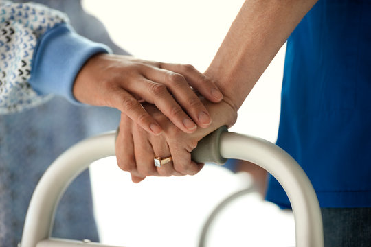 Nurse lays a supporting and comforting hand atop a young male patient's hand as he learns to walk again.