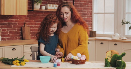 Mom and her little daughter are preparing for Easter. Happy family preparing painting Easter eggs in cozy kitchen