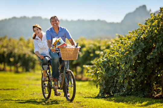 Happy mature couple riding their double bicycle through the vineyard.