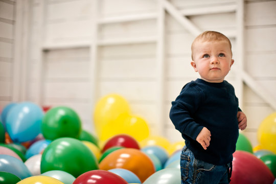 Little boy standing in a room full of balloons.