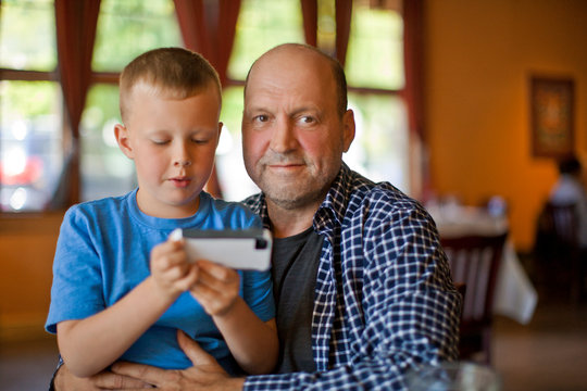 Portrait of a father with an arm around his son who is looking at a cell phone.
