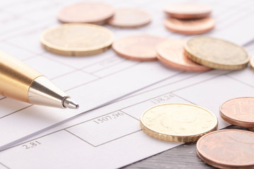 Stack of euro euro coins on old black wooden table. Pen and accounting documents with numbers