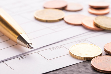 Stack of euro euro coins on old black wooden table. Pen and accounting documents with numbers