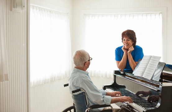 Happy senior man playing the piano while in a room with a nurse.