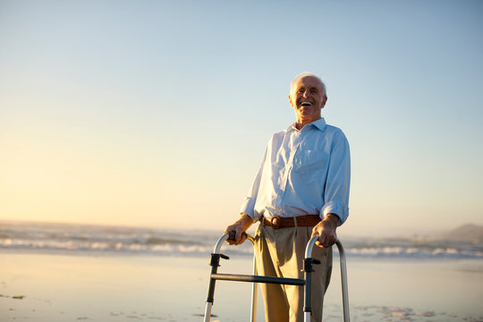 Portrait of a senior man standing on a beach with a walking aid.