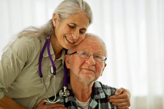 Doctor standing with her arms around an elderly patient.