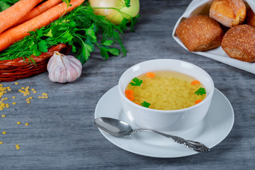 Chicken soup in bowl of broth and fresh vegetables on wooden table