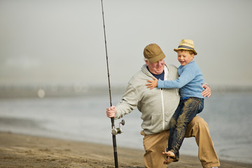 Senior man playing on a beach with his young grandson.