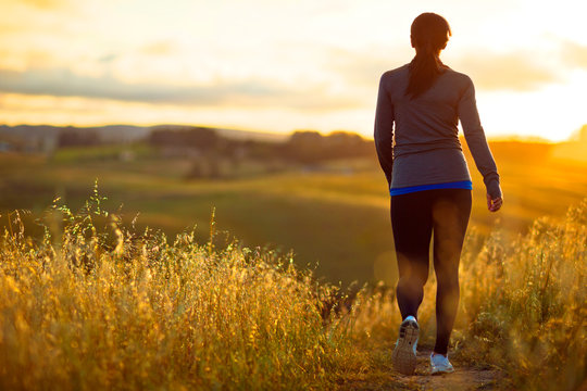 Energetic young woman jogging through the rural countryside at sunset.