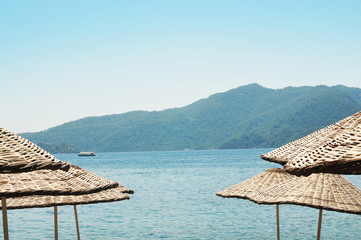Straw ambrellas on a beach with sea and mountains against clear sky