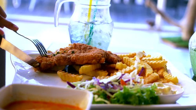 Chicken schnitzel, served with french fries and salad. someone eats french fries with a fork in a restaurant.