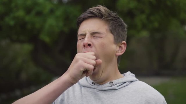 Bored, tired, young white teenager yawning whilst isolated outdoors in his backyard