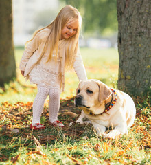 Cute little blonde girl sitting with dog on the grass in the forest