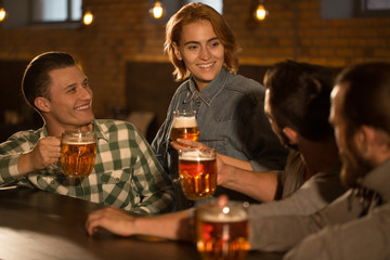 Company of handsome man and beautiful red haired woman in beer pub. Beautiful female client smiling and spending time with friends. People in bar holding beer glasses.