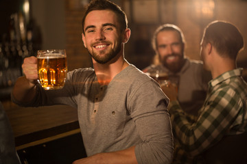 Positive men showing beer glasses they holding in hands. Male clients looking at camera, posing and smiling. Three cheerful men enjoying weekend in beer pub.