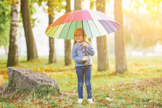 The image of a little girl with a rainbow umbrella in park