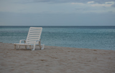 A White Beach Chair on the Beautiful Sunset Beach. Ahtlantic Ocean on a Background