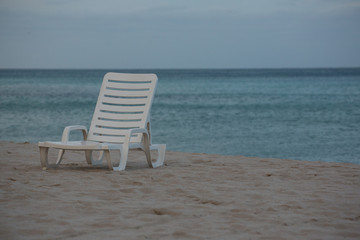 A White Beach Chair on the Beautiful Sunset Beach. Ahtlantic Ocean on a Background