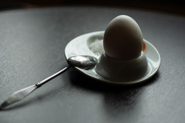 boiled egg with spoon, stand and salt on dark