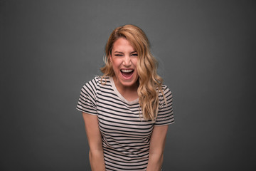 Emotional blonde screams. Girl straining screams standing on a gray background.