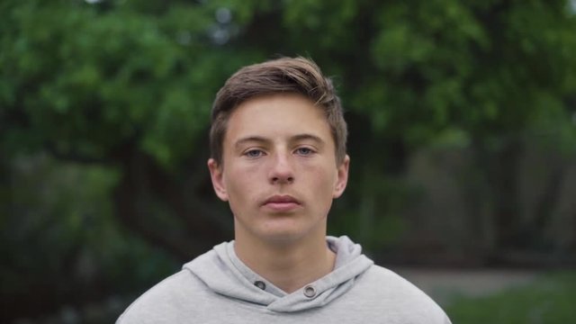 A young white boy teenager looking up into the camera and confidently staring whilst outdoors