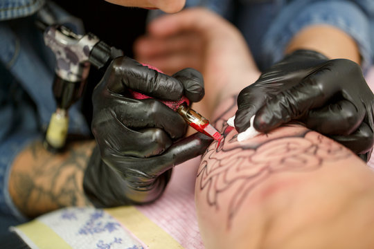 Close up of tattoo machine. Tattoer holding professional instrument in hand and making picture on client's hand. Tattoo master wearing black gloves. Tattooist working with tattoo needle and ink.
