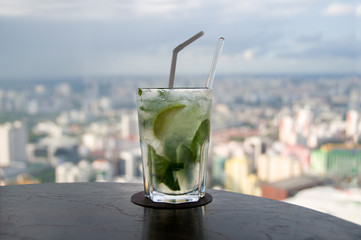 Mojito cocktail of mint leaves and lime with modern cityscape on the background