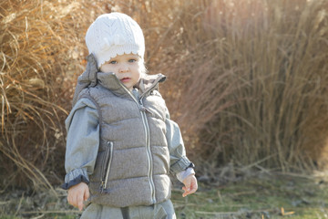  Outdoor portrait of an adorable girl wearing a white wool hat and warm clothes in a park 