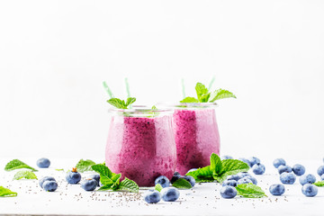 Purple homemade yogurt or smoothie with blueberries, chia seeds and mint leaves in glass jars on gray background, selective focus
