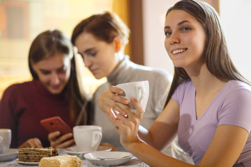 Girl holding cup of coffee in hand while sitting at table at cafe.