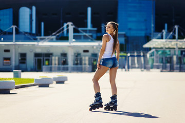 Portrait of a beautiful sexy young blonde girl on roller skates, in denim shorts and a T-shirt. Smiling and lookind at camera. Hot summer day. Outdoor city sports. Healthy lifestyle concept