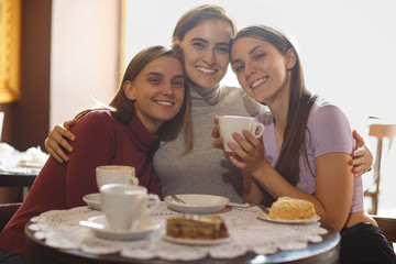 Three women sitting together in cafe and embracing with each other.