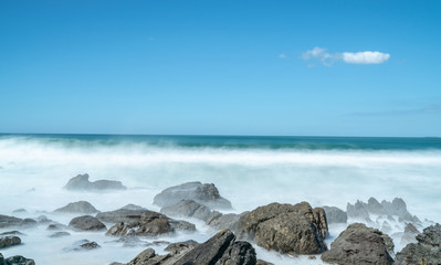Waves smoothed by long exposure washing in around rocky foreshore.