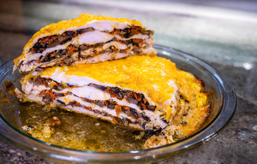 Appetizing Baked Meat Pie with mushrooms and vegetables topped with melted cheese is on the table in glass tray