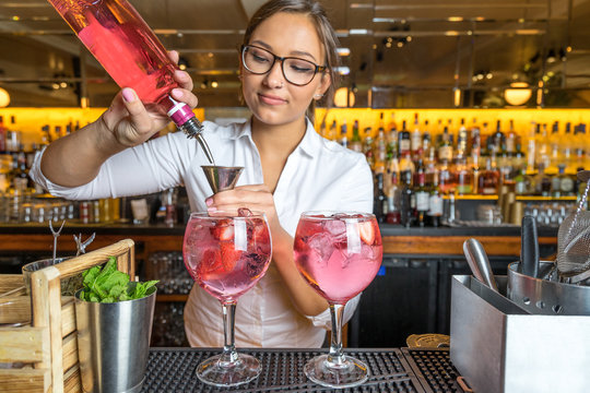 female beautiful smart bartender mixologist bar person makes prepares gin tonic cocktail drink pink mint fish bowl glass