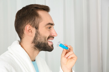 Young man using teeth whitening device on light background. Space for text