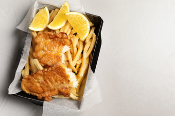 Container with British traditional fish and potato chips on light background, top view. Space for...