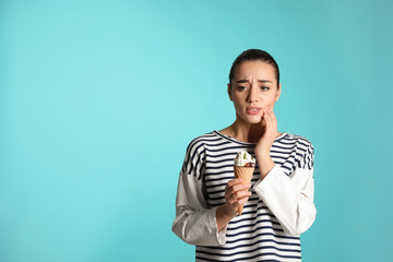 Fototapeta premium Emotional young woman with sensitive teeth and ice cream on color background. Space for text