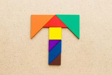 Tangram puzzle in alphabet letter T shape on wood background
