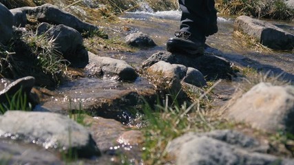 Small female feet in boots crossing a mountain rill in the Carpathians in slo-mo