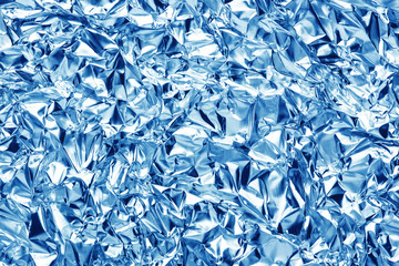 Silver crumpled metal foil texture. Blue color metal glossy surface background.