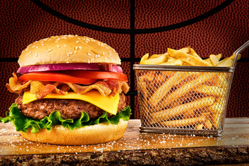 Cheeseburger with bacon and a basket of french fries. Basketball ball image in background.
