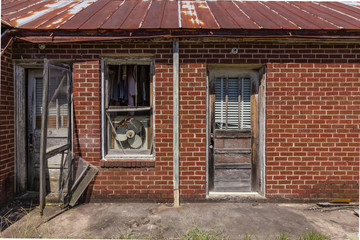 Abandoned red brick building with tattered wooden front door and rusted tin roof