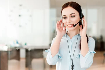 Foto op Plexiglas Friendly young female technical support dispatcher with a headset working in a call center on a hotline, talking on the phone. Portrait of an attractive customer care representative. Business concept © Anastasia