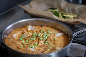 fish curry cooking in pan with baked courgettes in background