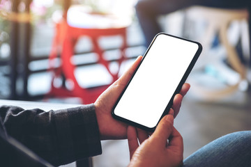 Mockup image of hands holding black mobile phone with blank white desktop screen in cafe