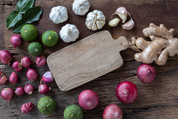 Top view of herbal vegetable ingredients, garlic, red onion, lime, lime leaf and chopping board on old wooden table, cooking preparation concept