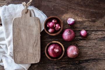 Top view of herbal vegetable ingredients, fresh red onion and empty chopping board on old wooden table, cooking preparation concept