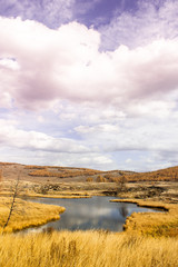 Autumn lake with mountain range on horizon. Valley with yellow dry grass