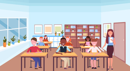 Fototapeta premium woman teacher reading book during lesson mix race pupils sitting desks education concept modern school classroom interior horizontal flat